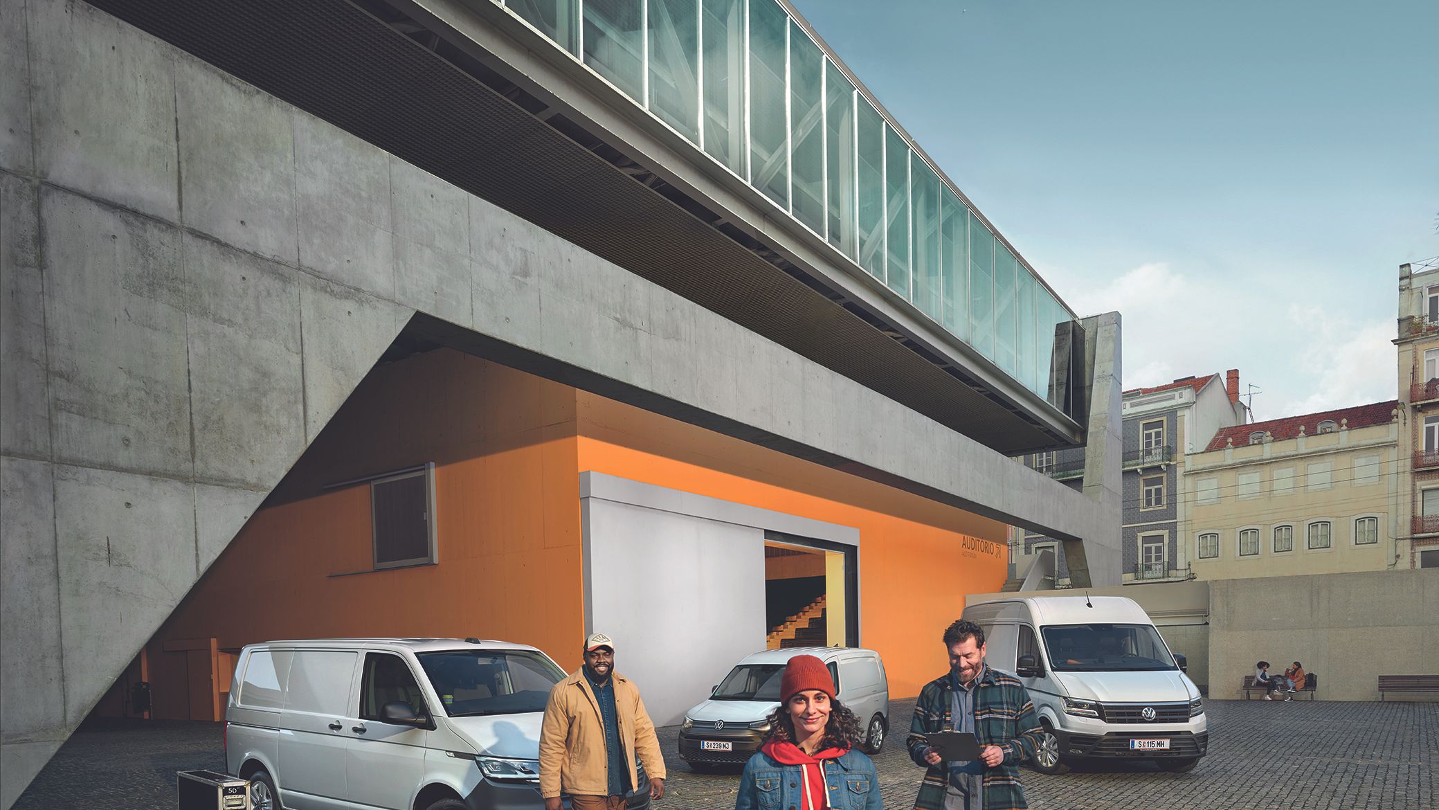 Furgoni i bardhë Crafter, Caddy Cargo e bardhë dhe Furgoni i bardhë i transportit janë parkuar në një parking përpara një ndërtese.
